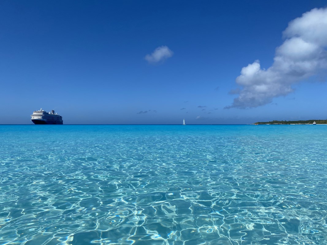 Une belle photo de paysage qui affiche les eaux cristallines de l'océan, avec un bateau de croisière sur le côté gauche de la ligne d'horizon.